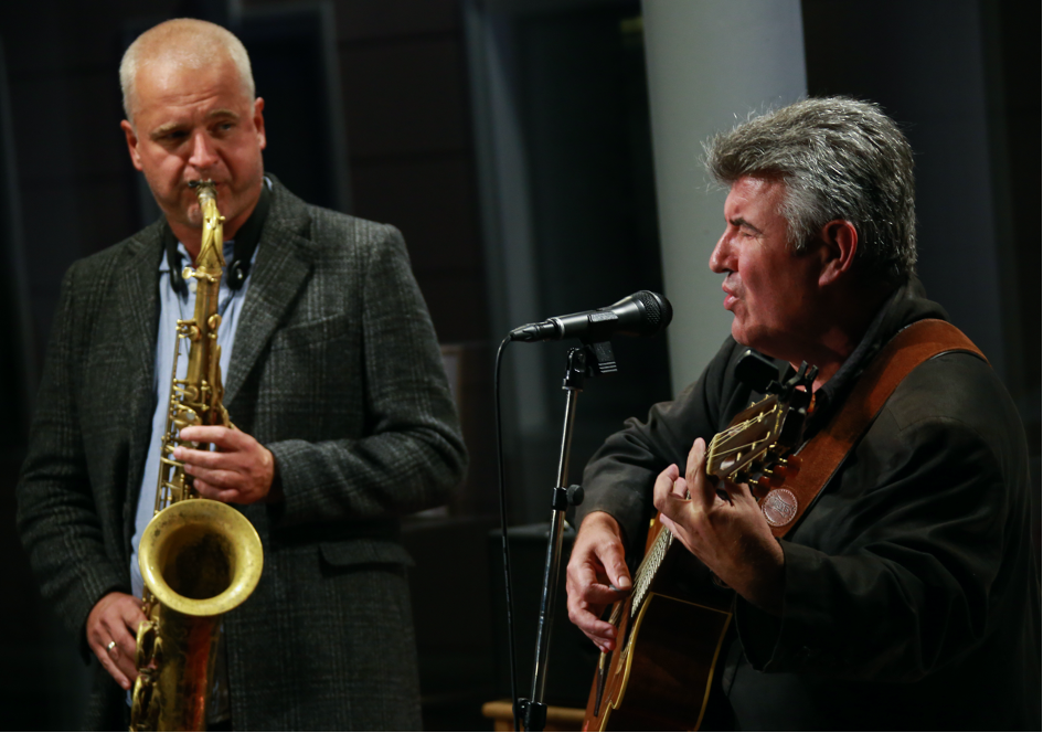 Ballet corps in white tutus performs synchronized movements with lead dancer centered, against turquoise-lit stage backdrop.