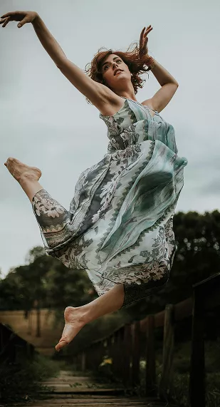 Ballet partners perform on stage under purple lighting, ballerina en pointe with arms raised, male dancer supporting beside her.